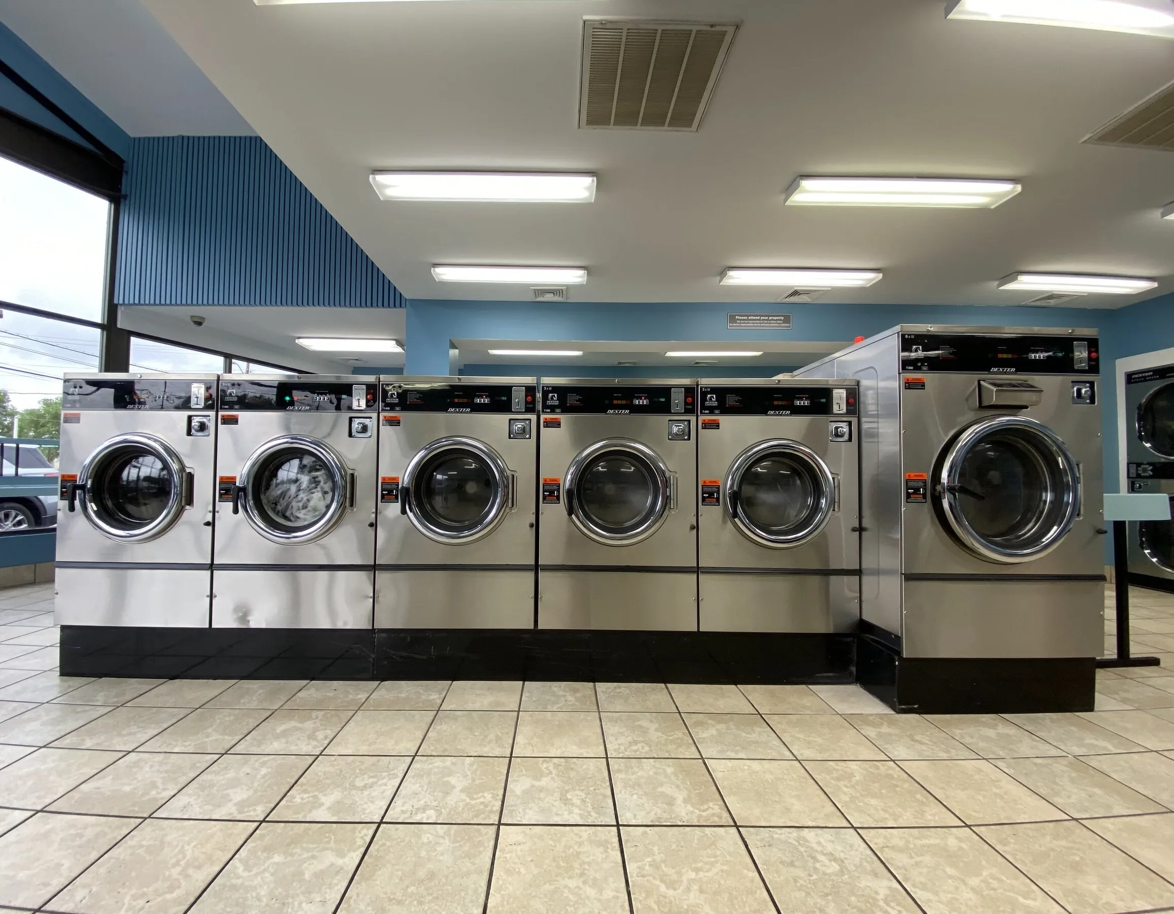 A row of front-load washers in bright daylight, with the parking lot visible through the windows.