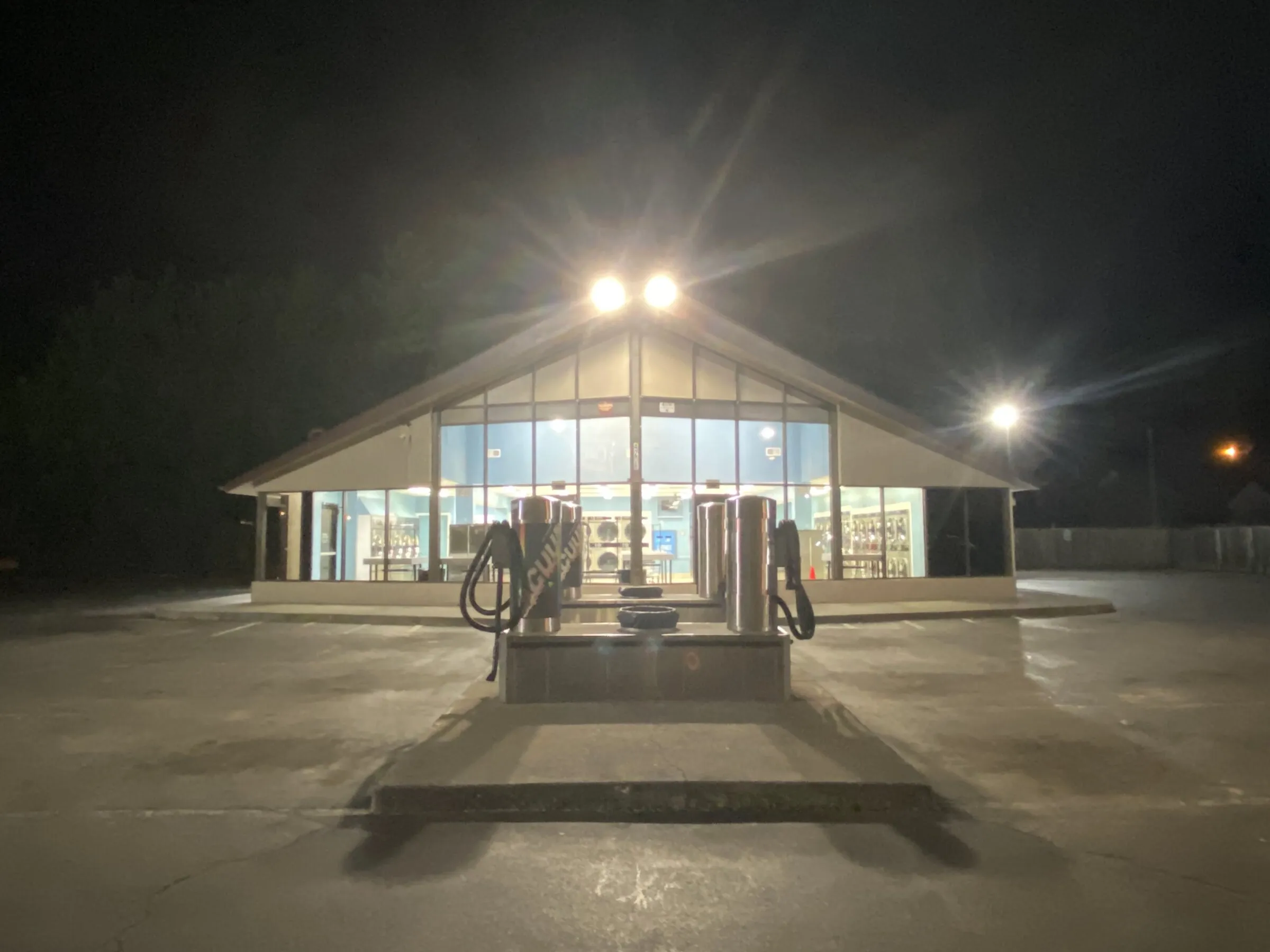 The car vacuums in the parking lot at night, with the store lit behind them.